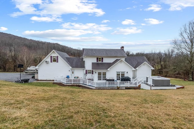 rear view of property with a jacuzzi, a chimney, a forest view, and a lawn