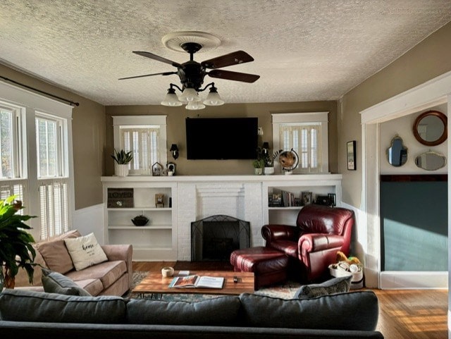 living room featuring ceiling fan, a fireplace, hardwood / wood-style floors, and a textured ceiling