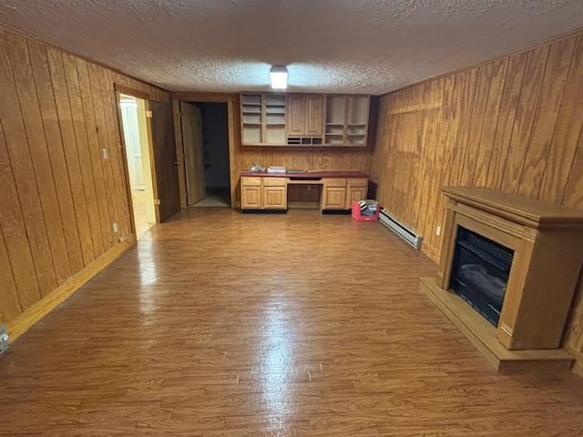 319 Bogey Dr, Abingdon, VA 24211 - unfurnished living room featuring wood finished floors, a textured ceiling, wooden walls, a glass covered fireplace, and a baseboard heating unit