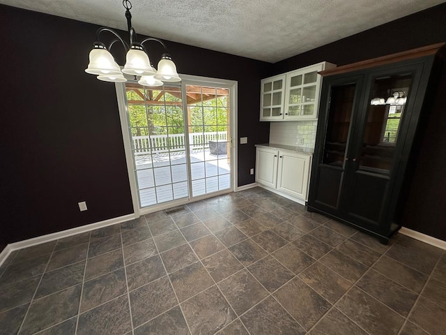 unfurnished dining area featuring a chandelier, baseboards, and a textured ceiling