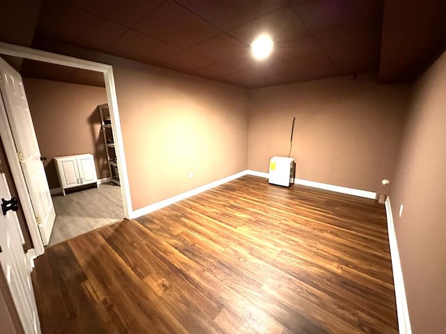 empty room featuring wood finished floors, baseboards, and a paneled ceiling