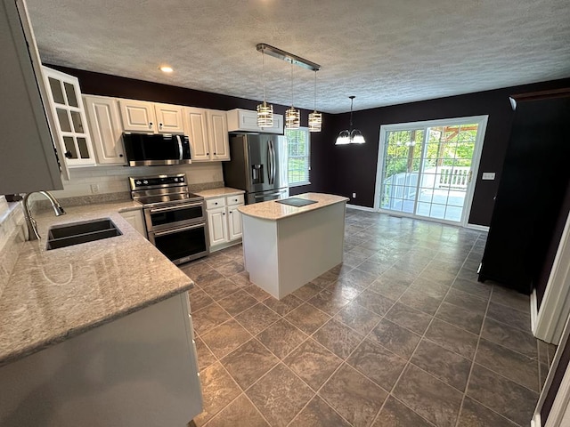 kitchen with appliances with stainless steel finishes, a sink, a center island, white cabinets, and a textured ceiling