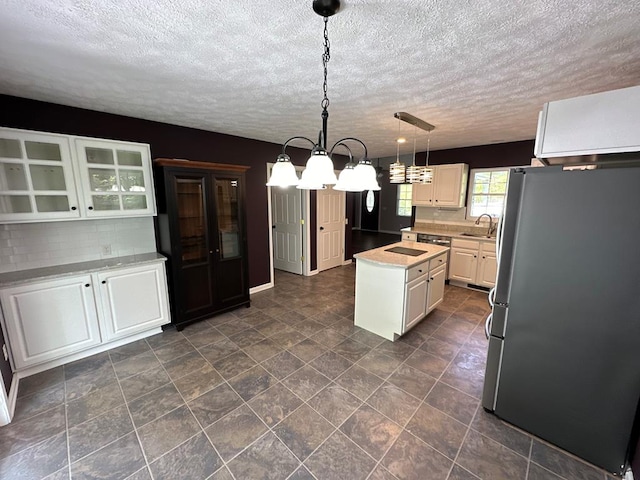 kitchen with freestanding refrigerator, a sink, light countertops, a kitchen island, and a chandelier