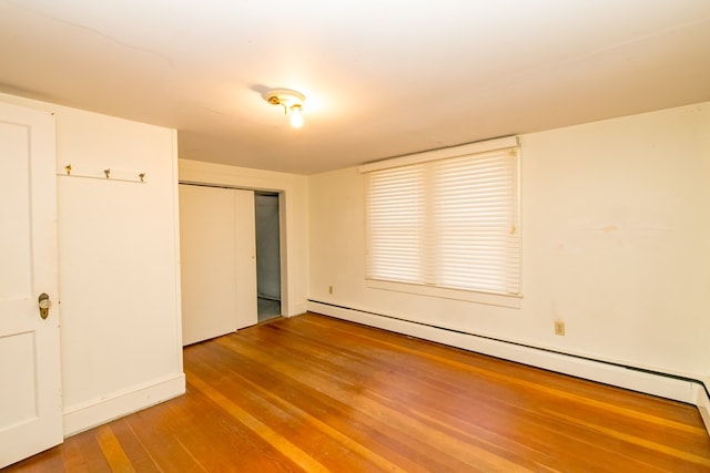 unfurnished bedroom with a baseboard radiator, wood-type flooring, and a closet