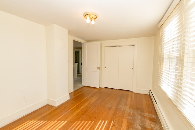 unfurnished bedroom featuring multiple windows, a baseboard radiator, wood-type flooring, and a closet