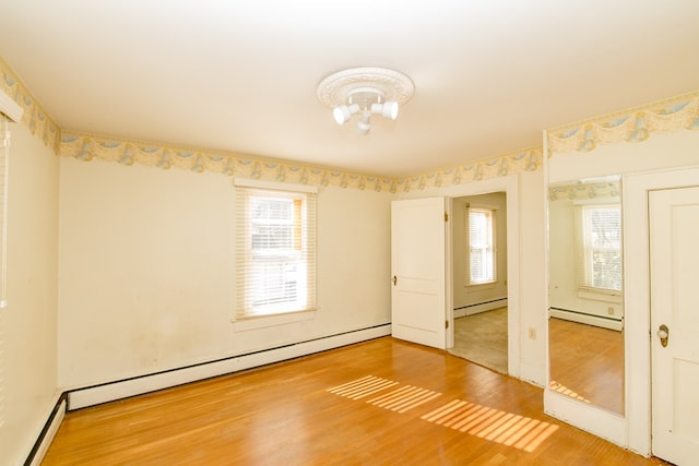 empty room with a baseboard radiator, a healthy amount of sunlight, and hardwood / wood-style floors