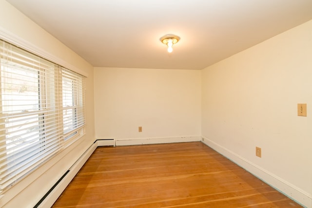 empty room featuring wood-type flooring and a baseboard heating unit