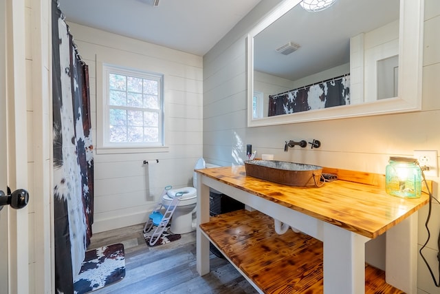 bathroom with wood-type flooring, toilet, sink, and wood walls