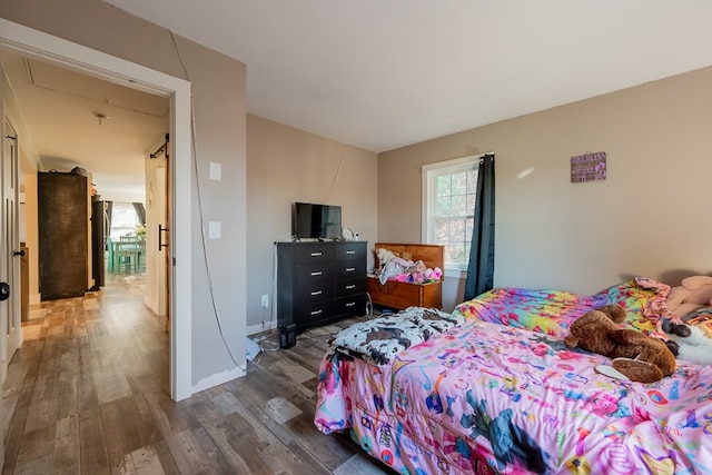 bedroom with a barn door and dark hardwood / wood-style flooring