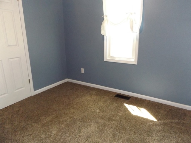 unfurnished room with baseboards, dark carpet, and visible vents