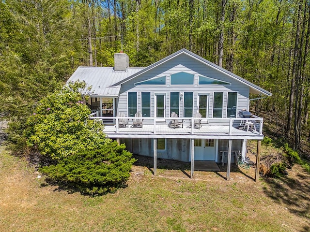 rear view of property with a wooden deck, a chimney, and a view of trees