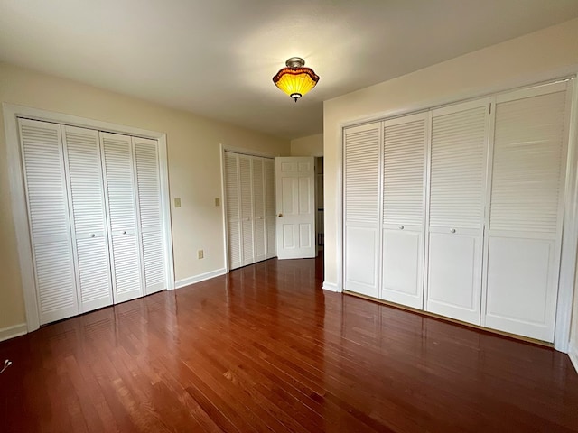 unfurnished bedroom with baseboards, multiple closets, and wood finished floors