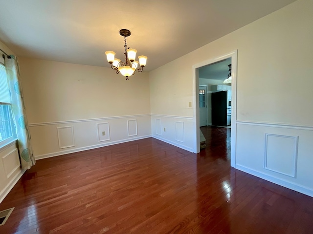 spare room featuring a wainscoted wall, visible vents, a chandelier, and dark wood finished floors