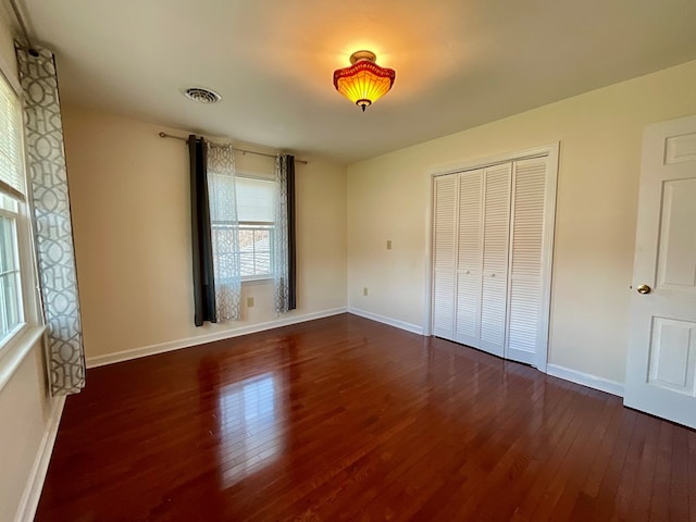 unfurnished bedroom with wood-type flooring, a closet, baseboards, and visible vents
