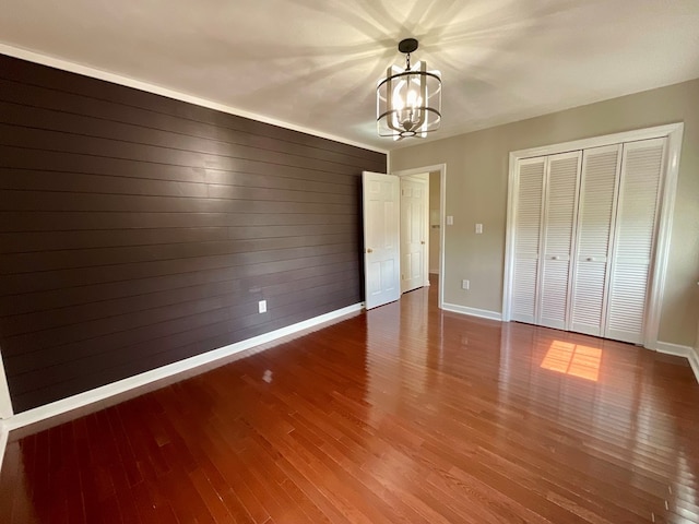 unfurnished bedroom with baseboards, wood finished floors, a closet, and a notable chandelier
