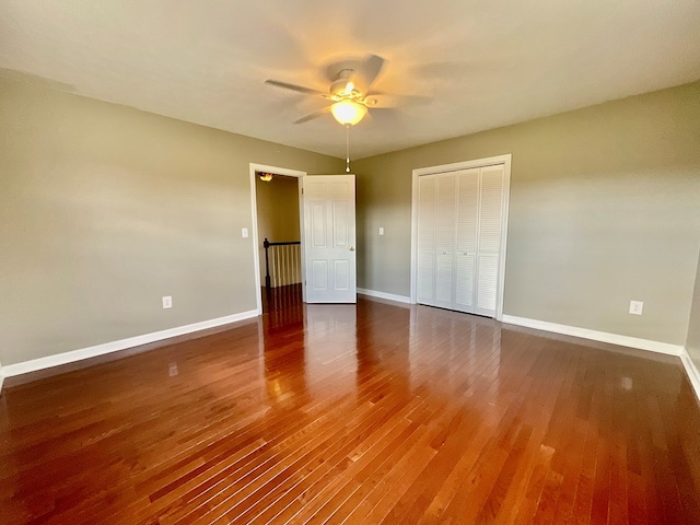 unfurnished bedroom with baseboards, wood finished floors, a closet, and a ceiling fan