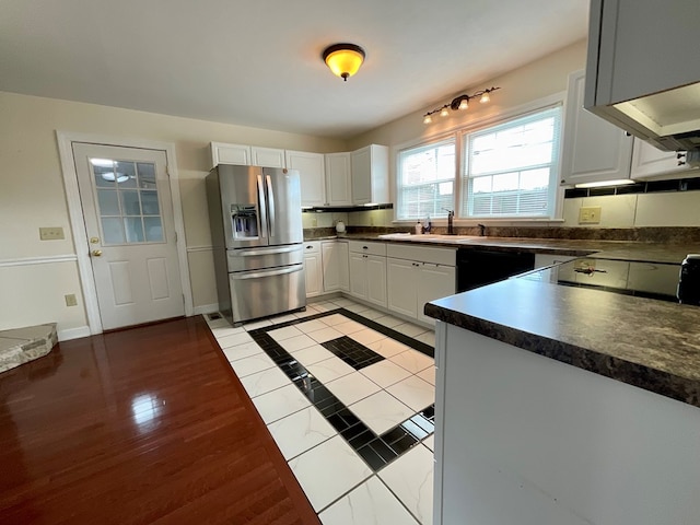 kitchen with dark countertops, black dishwasher, white cabinetry, a sink, and stainless steel fridge with ice dispenser