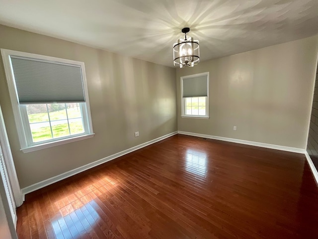 empty room featuring baseboards, dark wood-style flooring, a wealth of natural light, and a chandelier