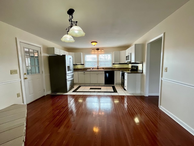 kitchen with a sink, black appliances, wood-type flooring, dark countertops, and decorative light fixtures