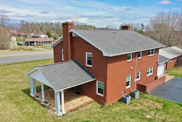 exterior space with cooling unit, driveway, a yard, and a chimney