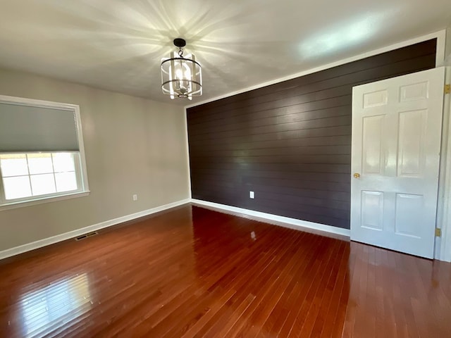 empty room featuring wood walls, visible vents, baseboards, wood finished floors, and an inviting chandelier