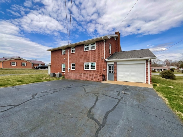 view of side of home featuring an attached garage, central AC, brick siding, driveway, and a yard