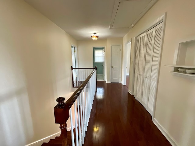 hall featuring an upstairs landing, dark wood-type flooring, attic access, and baseboards