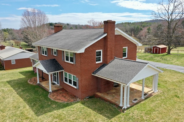 exterior space featuring roof with shingles, a chimney, a shed, an outbuilding, and a yard
