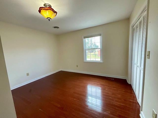 unfurnished bedroom featuring visible vents, a closet, baseboards, and dark wood finished floors