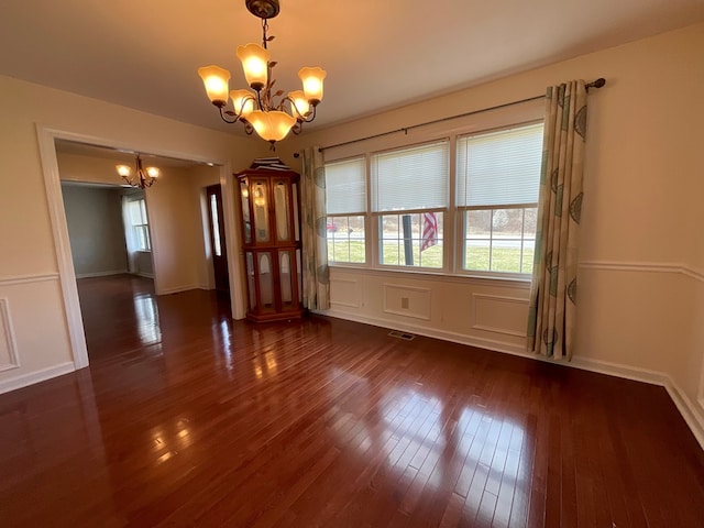 unfurnished room with dark wood-type flooring, visible vents, baseboards, and a notable chandelier