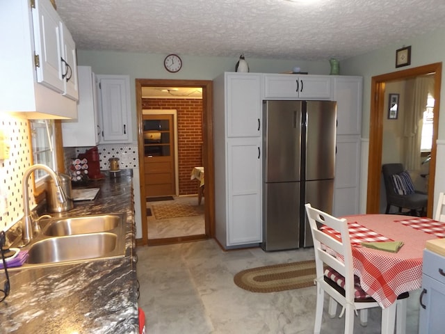 kitchen featuring sink, a textured ceiling, white cabinets, and stainless steel refrigerator