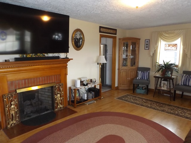 living room featuring a brick fireplace, wood-type flooring, and a textured ceiling