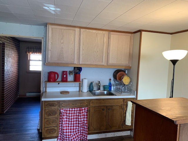 kitchen featuring dark wood-type flooring, light brown cabinetry, sink, brick wall, and a baseboard heating unit