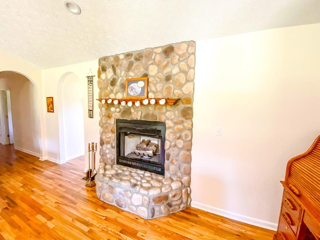 1476 E Blue Grass Trl, Bland, VA 24315 - unfurnished living room with arched walkways, a textured ceiling, wood finished floors, baseboards, and a stone fireplace
