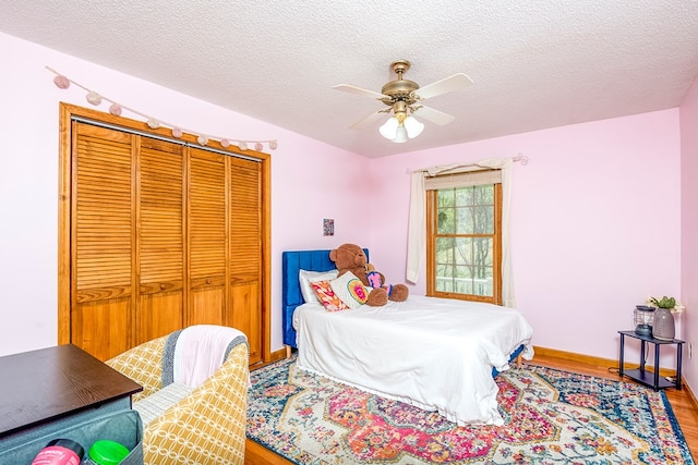 bedroom featuring a textured ceiling, baseboards, wood finished floors, a closet, and ceiling fan