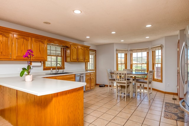 kitchen with brown cabinets, recessed lighting, stainless steel dishwasher, a sink, and a peninsula