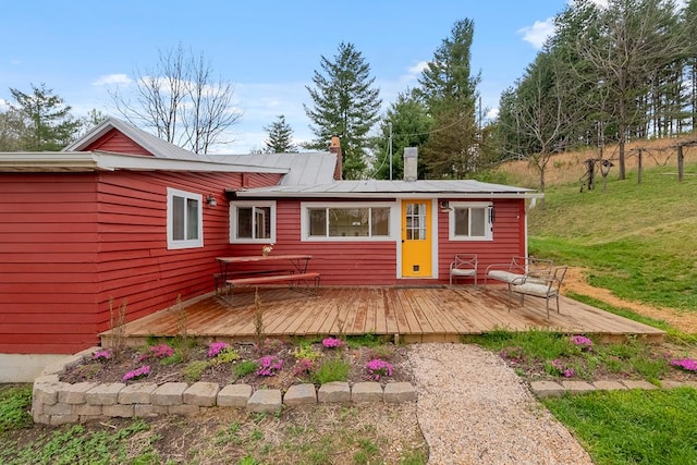 rear view of house with a chimney, a deck, and a yard