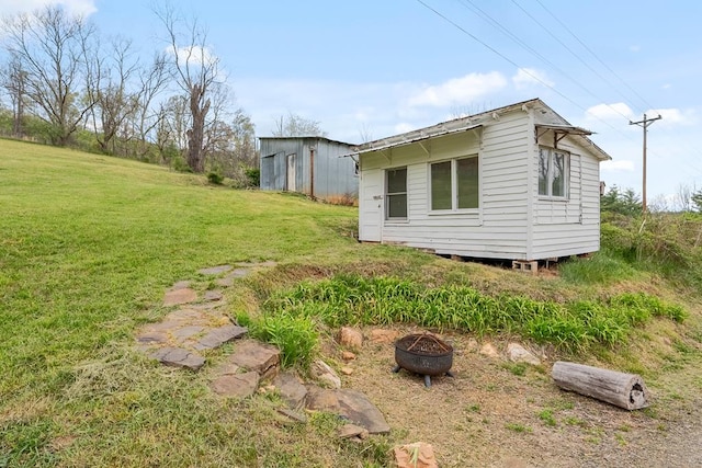 view of side of property with a lawn, an outdoor structure, and a fire pit