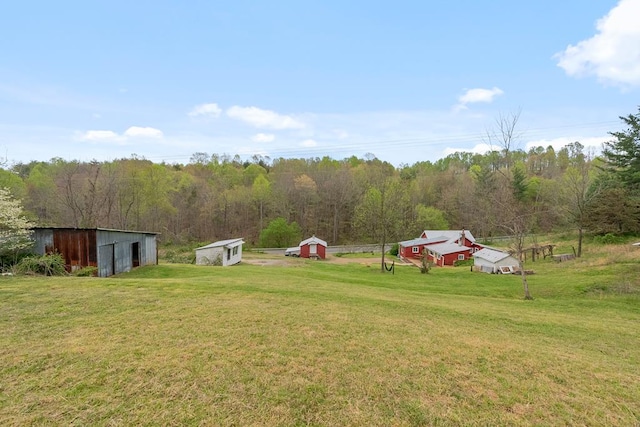 view of grassy yard featuring an outdoor structure, an outbuilding, and a forest view