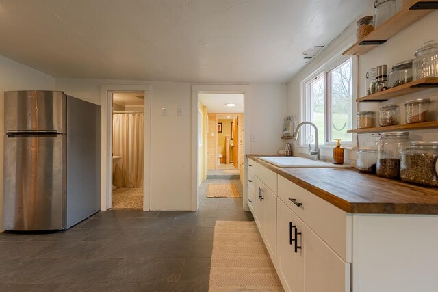 kitchen featuring freestanding refrigerator, a sink, white cabinets, open shelves, and wooden counters