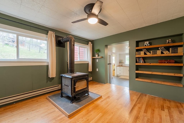 miscellaneous room featuring wood finished floors, ceiling fan, a baseboard radiator, and a wood stove