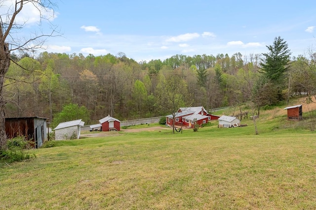 view of green lawn featuring a storage shed, an outbuilding, and a view of trees