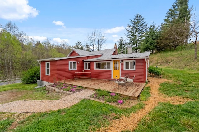 back of property featuring a chimney, a wooden deck, a yard, and metal roof