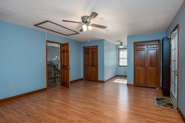 unfurnished bedroom featuring baseboards, light wood-style floors, attic access, and a textured ceiling