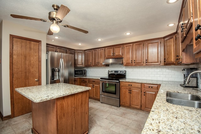 kitchen featuring backsplash, light stone countertops, under cabinet range hood, stainless steel appliances, and a sink