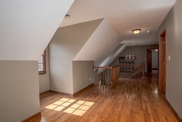 bonus room featuring a notable chandelier, a textured ceiling, baseboards, and wood finished floors