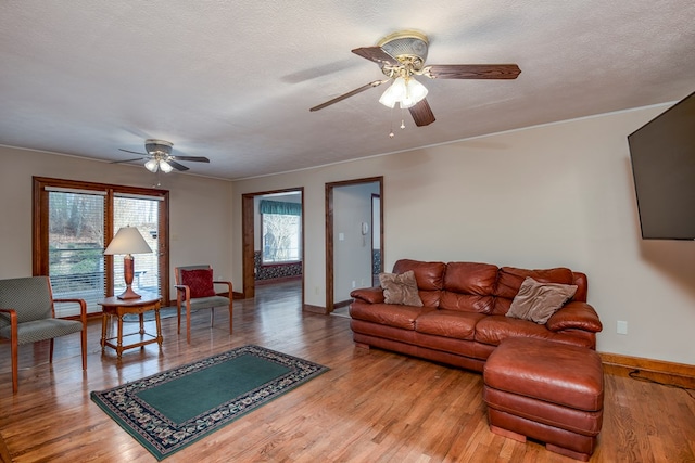 living room featuring a ceiling fan, wood finished floors, baseboards, and a textured ceiling