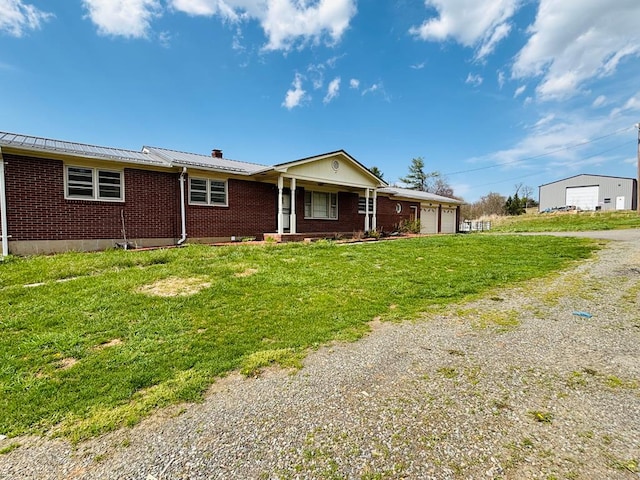 single story home with driveway, covered porch, brick siding, a front yard, and metal roof