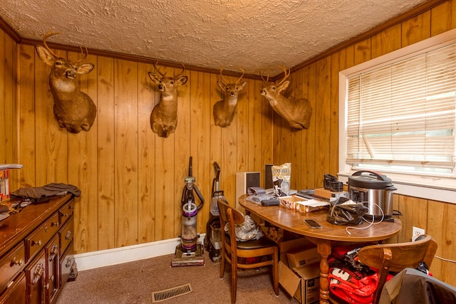 carpeted dining space featuring wooden walls, crown molding, a textured ceiling, and visible vents