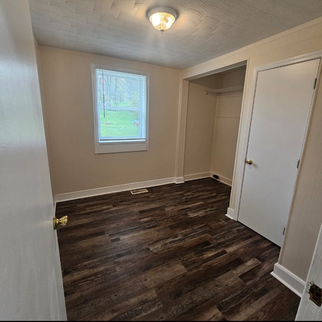 unfurnished bedroom with a closet, baseboards, visible vents, and dark wood-style floors